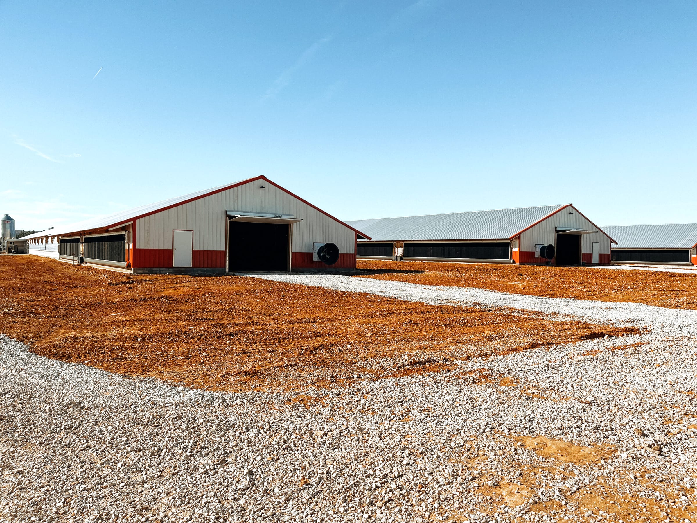 Two newly built poultry houses with red trim on a graded site